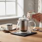 whb-superb Glasteekanne mit Edelstahl-Teesieb auf einem Schieferuntersetzer, neben einer Tasse und losem Tee.