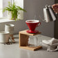 whb-superb HARIO V60 Kaffeefilter in Rot auf Holzständer mit Glaskanne beim Aufgießen von Filterkaffee