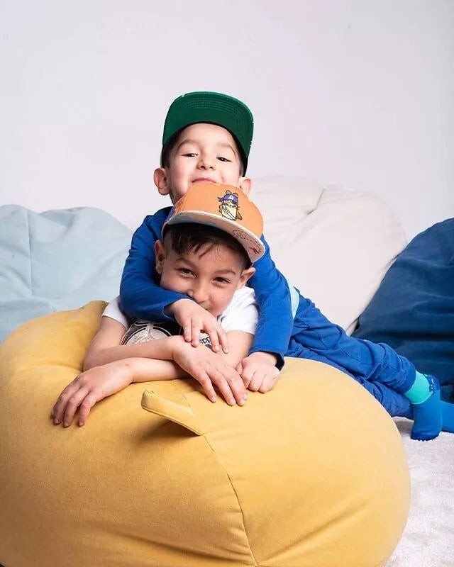 Zwei Jungen tragen koaa Snapback Kids Pirat Kappen mit Maus-Stickerei und Schatzkarten-Schirm auf einem Sitzsack