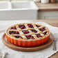 whb-superb Le Creuset Tarteform aus ofenrotem Steinzeug mit einer frisch gebackenen Beeren-Tarte auf einem Holzteller