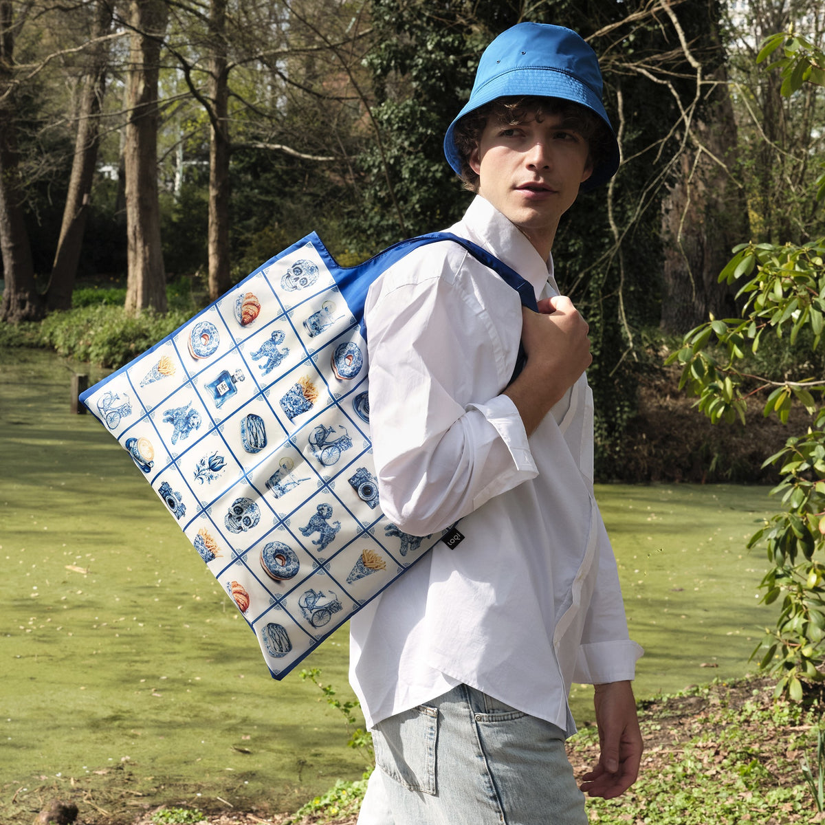 whb-superb LOQI Delft Heritage Tasche mit blau-weißem Kachelmuster, getragen von einem Mann mit blauem Fischerhut