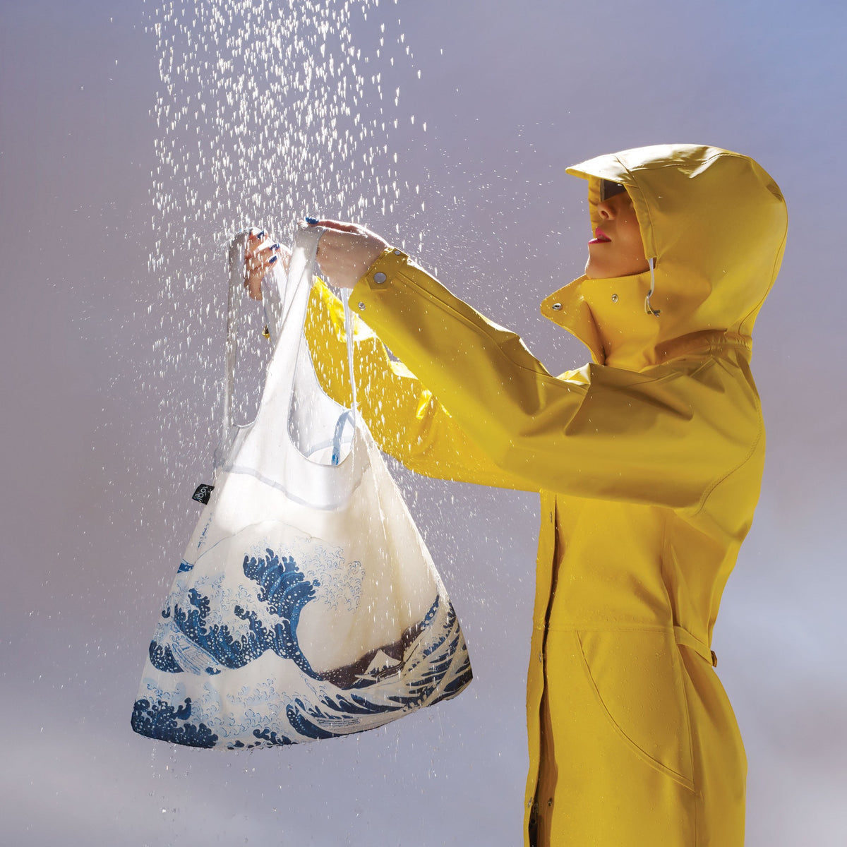 whb-superb LOQI Einkaufstasche Fuji aus recyceltem Taft in einer gelben Regenjacke unter Wasserstrahlen