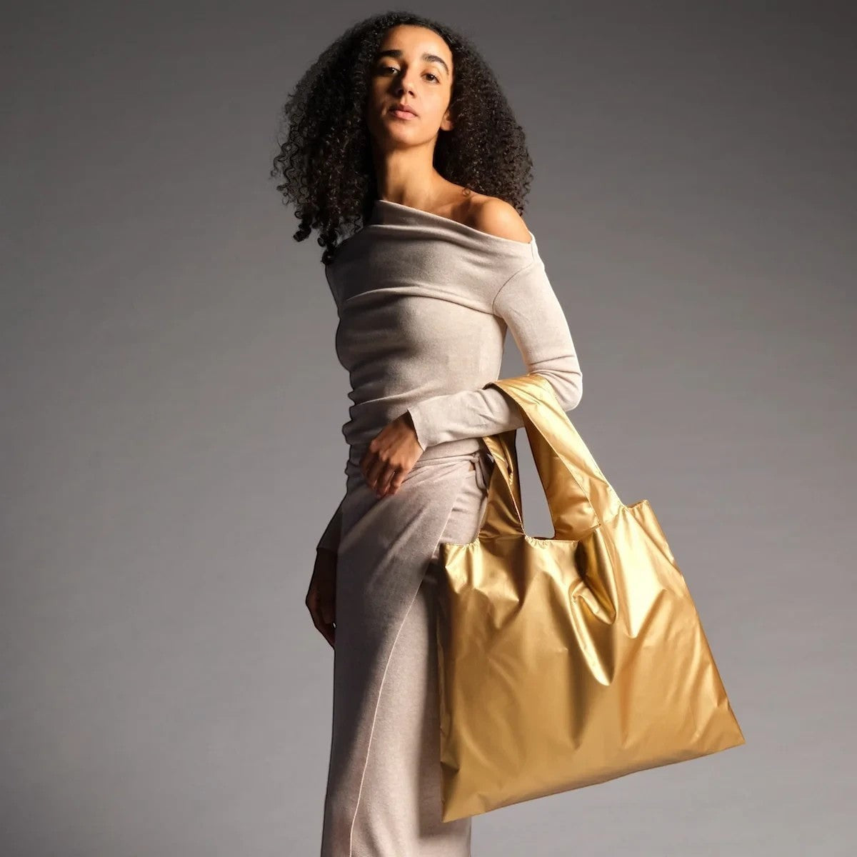 Model trägt eine goldene, matte LOQI Tragetasche aus wasserfestem Polyester vor einem grauen Hintergrund.