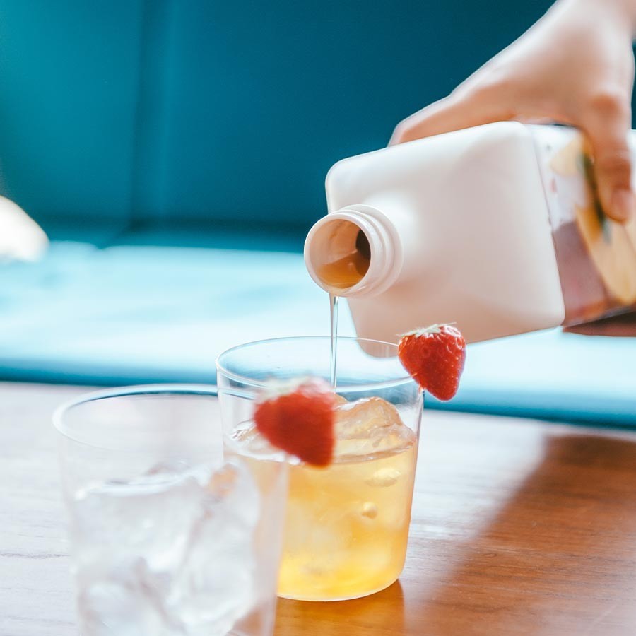 whb-superb weiße Teeflasche mit Filter 1200 ml, die in ein Glas mit Eis und Erdbeeren gegossen wird